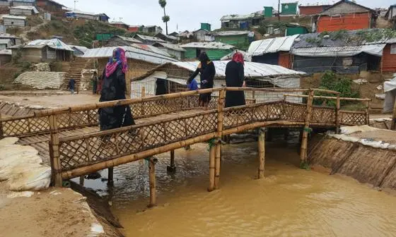 Women walking over a bamboo bridge in a refugee camp.