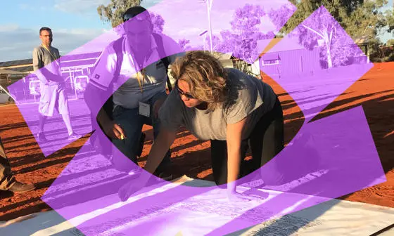 A woman on the floor looking at a large piece of paper.