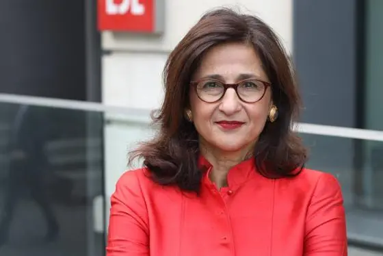 Minouche Shafik in a pink jacket standing in front of the LSE logo