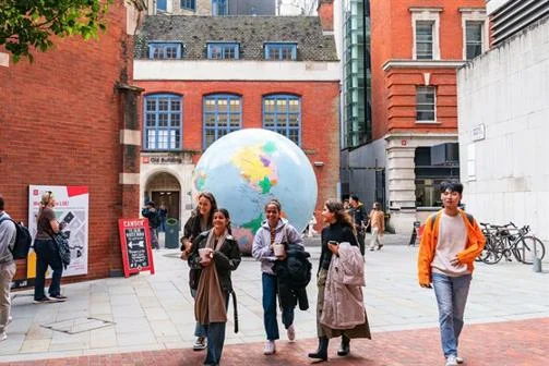 Students walking on campus in front of "The World Turned Upside Down" sculpture.