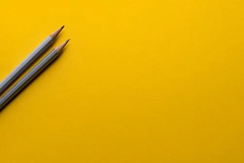 Two grey pencils on a yellow background