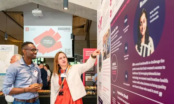 An LSE researcher speaking to a member of the public at the exhibition, pointing at one of the exhibits.
