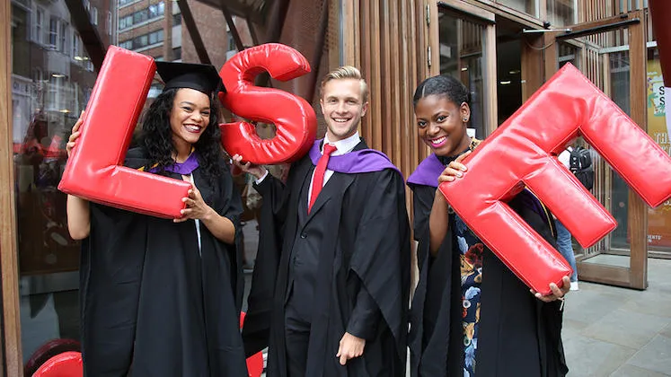 three students in black graduation robes holding up red LSE letters.
