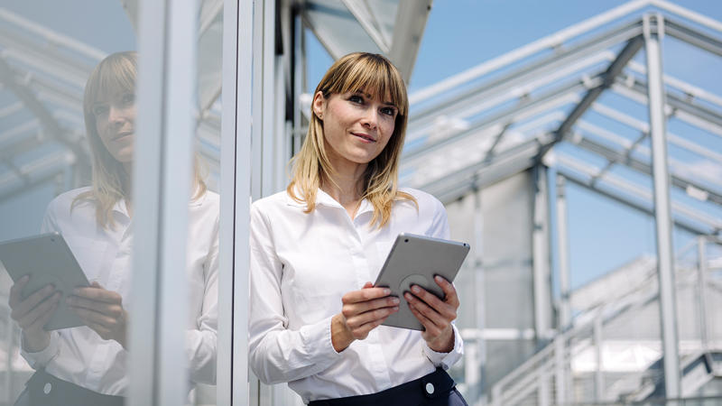 Thoughtful woman standing in front of building with tablet Social Entrepreneurship