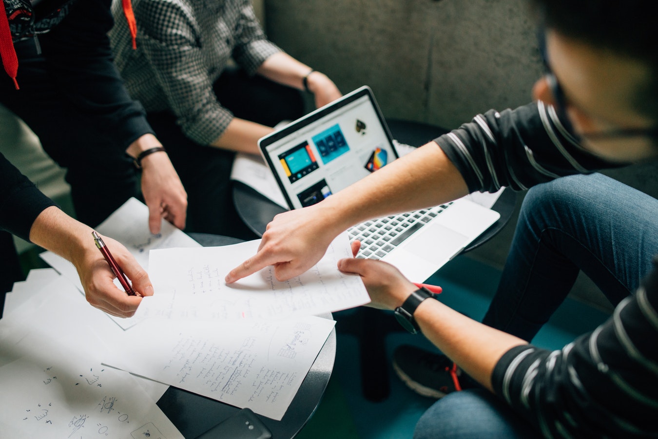 group of students sit around a laptop and point at pieces of paper