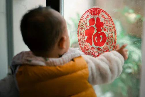 Child facing a window with Chinese decoration