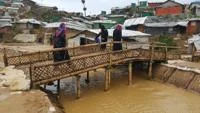 Women walking over a bamboo bridge in a refugee camp.