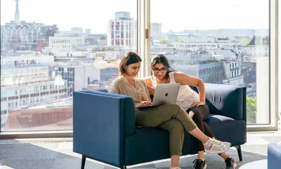 Two women sit in LSE's Centre Building looking at a laptop