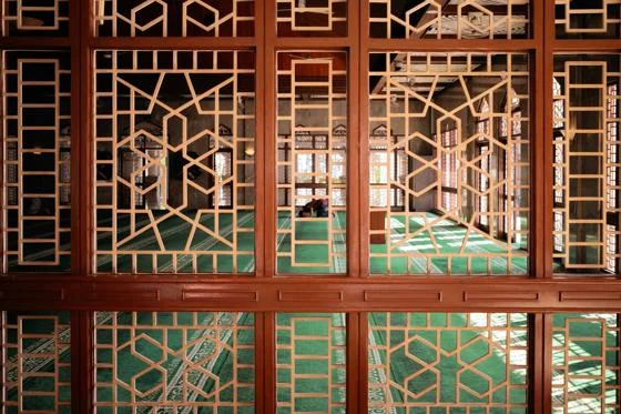Intricate wooden screens frame a mosques interior, where a man is praying