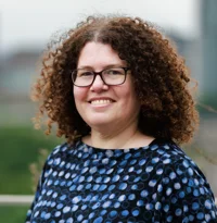headshot of a woman smiling at the camera, wearing a blue spotty top