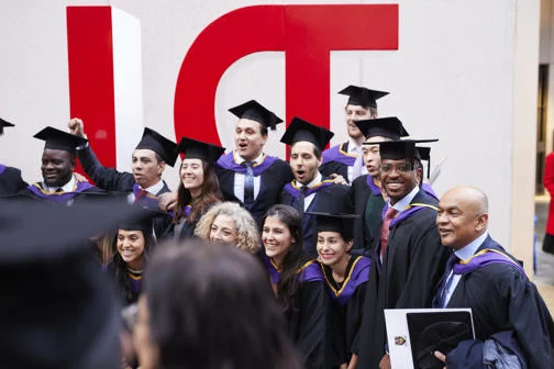 Students in graduation caps and gowns standing in front of the red LSE sign