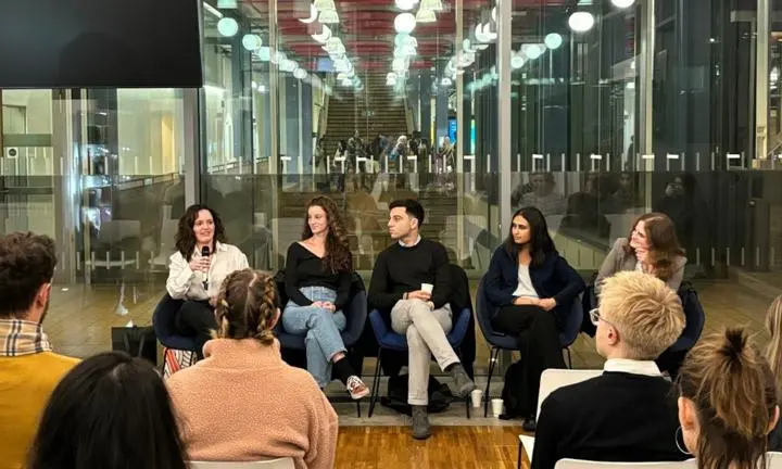 Five people sat in front an audience with a woman holding a microphone