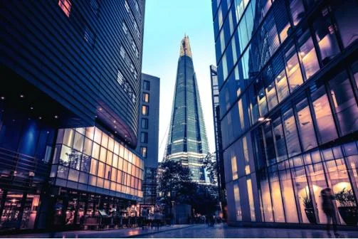 View of The Shard skyscraper in London framed by reflective glass buildings at dusk.