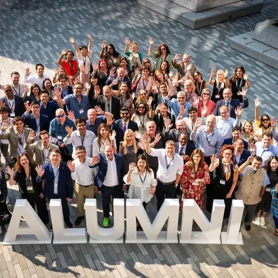 Many LSE alumni stand in the CBG square waving by some letters which spell "Alumni"