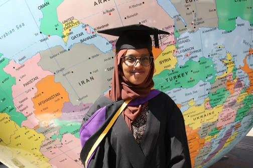 Graduating student wearing robes standing in front of LSE's globe
