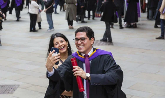 Male LSE graduate and female companion take a selfie in front of a crowd.