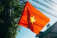 Vietnamese flag flying on a wooden mast near a building and a tree