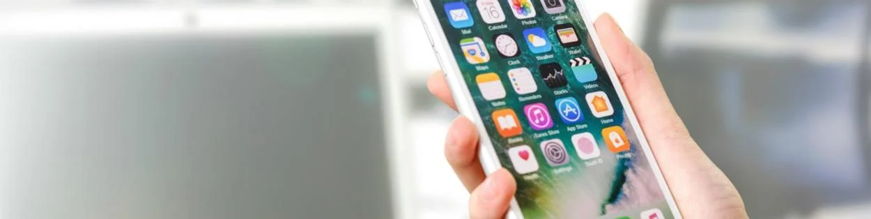 A person holding a mobile phone with various apps displayed.