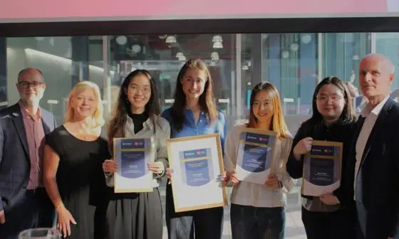 A group of four geography students posing with their certificates next to Chronos judges.