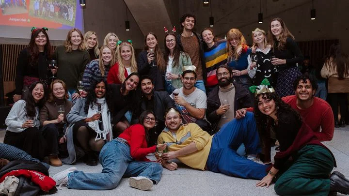 A group of master's students wearing festive headbands and smiling to camera.