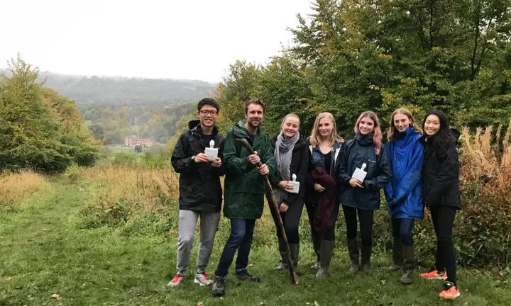 A group of students and staff posing with Juniper Hall in the background.