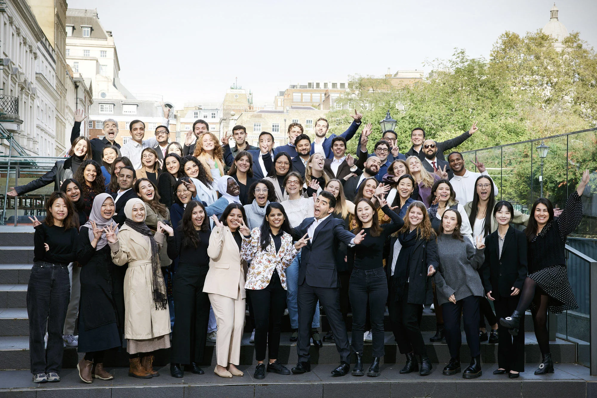 Group of students outside CKK building smiling with arms outstretched