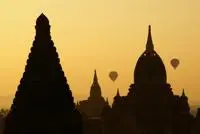 Three temples and two hot air balloons silhouetted against a yellow sky