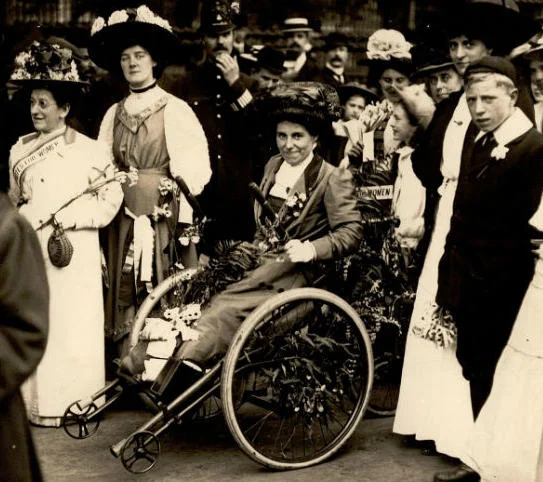 Rosa May Billinghurst sitting in her tricycle surrounded by people