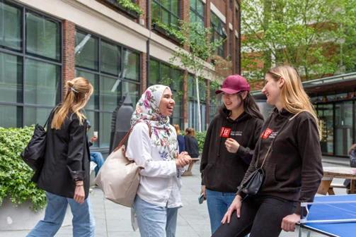 IRD female students laughing and chatting near library and table tennis table