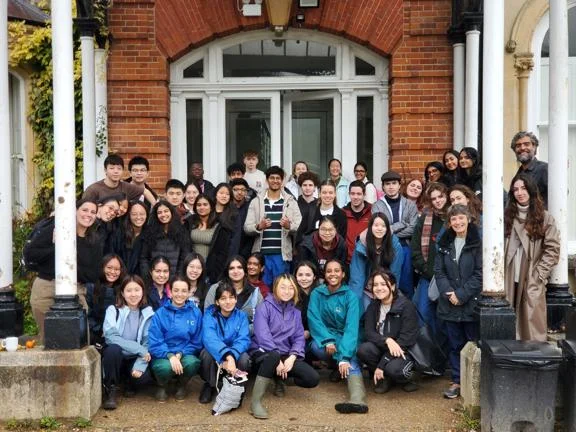 Students and staff standing and sitting next to a door with white pillars at the side.