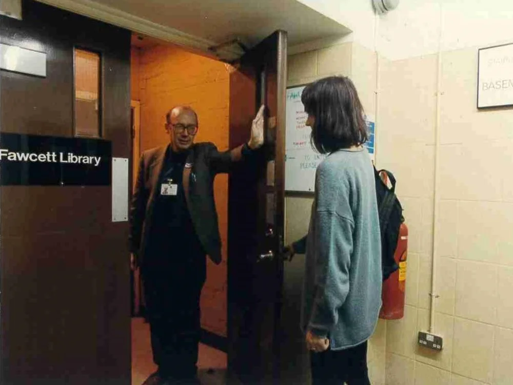 A person stood at the doors of the Fawcett Library welcoming someone.