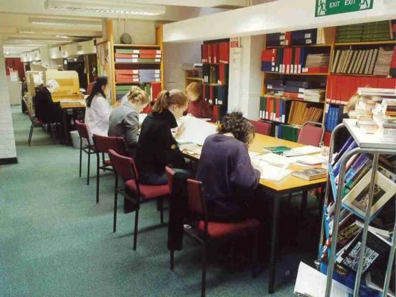Inside the Fawcett Library with people studying at desks and files on shelves.