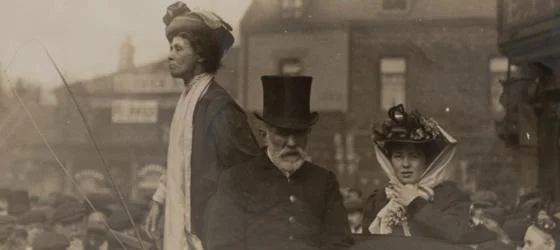A woman stood giving a speech with two others sat next to them.