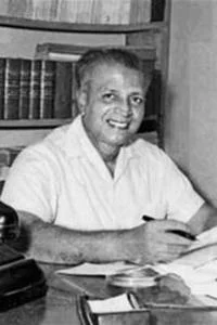 N M Perera sat at a desk smiling.