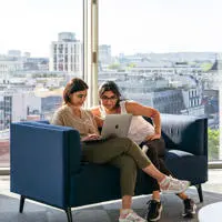 Two students sitting on a sofa, working at laptop.