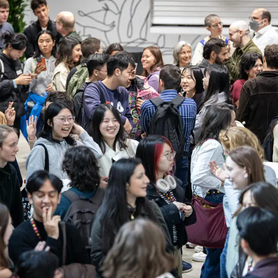 A group of students and staff stand in a room and talk