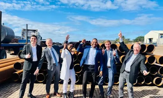 Six people in suits standing in front of copper coils in Mozambique. Deep blue sky.