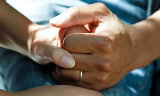 A man wearing a wedding ring holds a woman's hand.