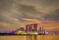 Singapore city skyline across body of water at night, with gold and pink hues
