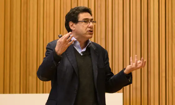Philippe Aghion stands giving a talk. Behind him is a wood panelled wall.