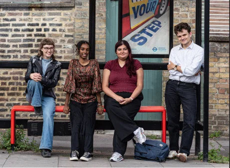 Four young people sitting and standing at a bus stop