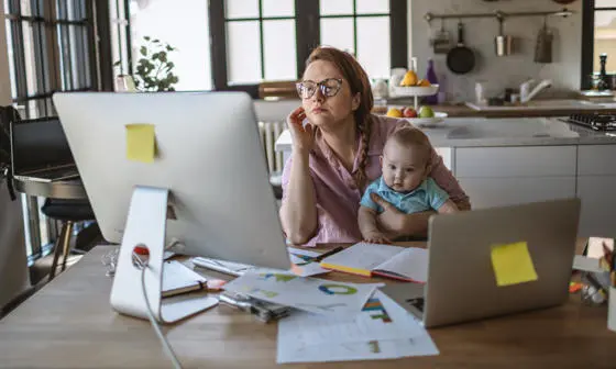 A woman works at a computer while holding a baby
