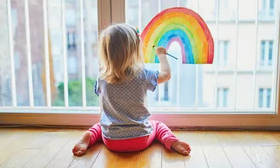 Child painting rainbow on window