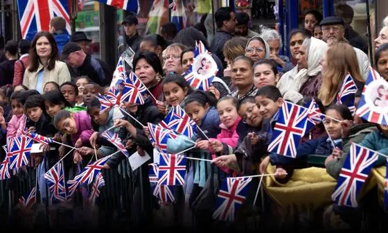 A diverse group of adults and children waving Union Jacks at an open air event