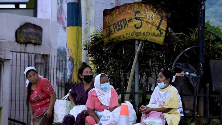 Women sell vegetables under a sign in Spanish and Nahuat