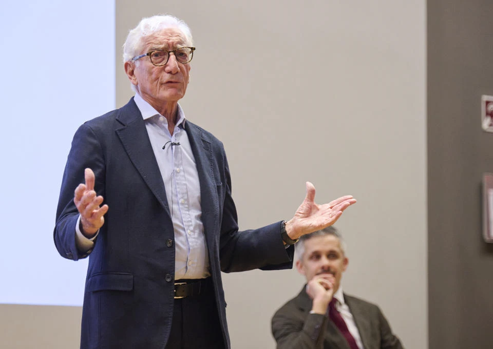 Man in a suit delivering a lecture with slides projected behind him