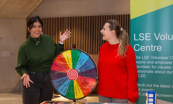 Two students stand with a colourful rainbow spinning wheel