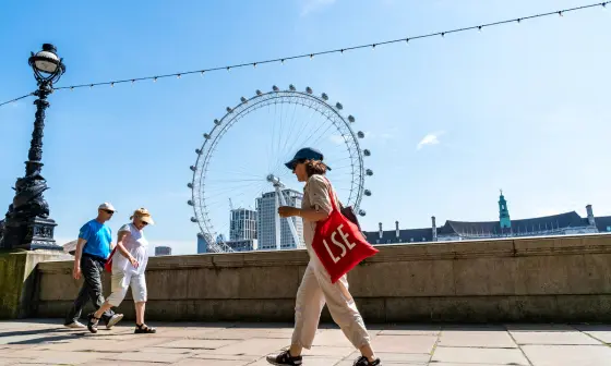 Woman walking opposite the London eye carrying a red LSE tote bag
