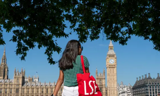 A woman sitting across from Houses of parliamnet with a red LSE tote bag