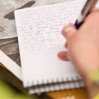 hand writing in a notebook with a pen